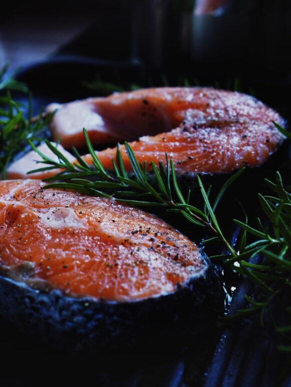 Alt-text: Two cuts of raw fish with rosemary on a platter. 
